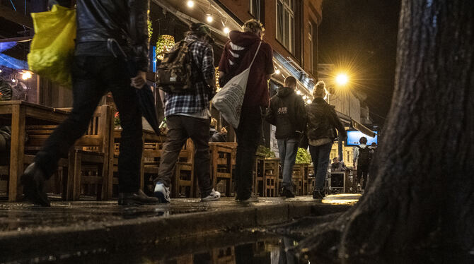Menschen gehen gegen Mitternacht an Kneipen vorbei
