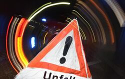 Ein Warndreieck mit dem Schriftzug »Unfall« steht vor einem Blaulicht auf der Straße.