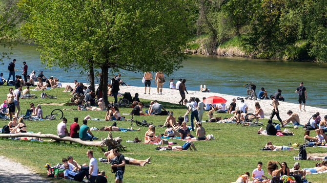 Viele Menschen lagern am Sonntag auf einer Wiese am Ufer der Isar und genießen das sommerlich warme Wetter.