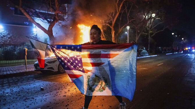 Einwanderung, Demonstrationen, Konflikte, Unruhen, Migration, Militär, Regierung Los Angeles: Eine Frau mit mehreren Flaggen geht an einem brennenden Auto vorbei, während sie gegen die Razzien der Trump-Regie
