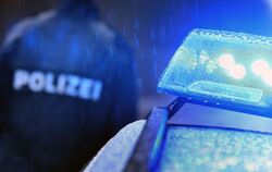 Ein Polizist steht an einem Streifenwagen, an dem das Blaulicht leuchtet.