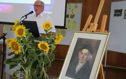 Vorsitzender Dieter Sigler bei seiner Festred. Im Vordergrund ein Bild von Samuel Hahnemann, dem Begründer der Homöopathe. 