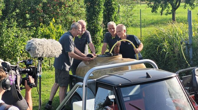 Reiner Gaub, Joachim Funk und Martin Wörnle (von links nach rechts) befüllen zusammen mit SWR-Reporter Harry Röhrle das Wasserfa