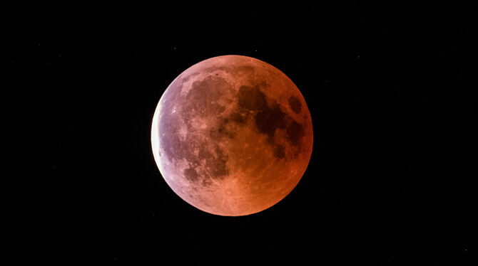 Der teilweise vom Erdschatten verdunkelte Vollmond leuchtet während einer Mondfinsternis rötlich.
