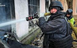 Feuerwehrmänner in Stahlhelmen und Splitterschutzwesten: Ein Bild von Löscharbeiten nach einem Angriff auf ein Werkstattgebäude