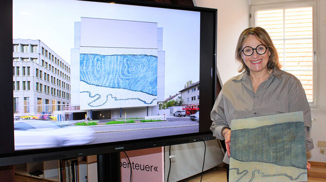 Tanja Niederfeld zeigt ihren Holzschnitt vor einer Präsentation der Fassade, auf die er übertragen wurde.